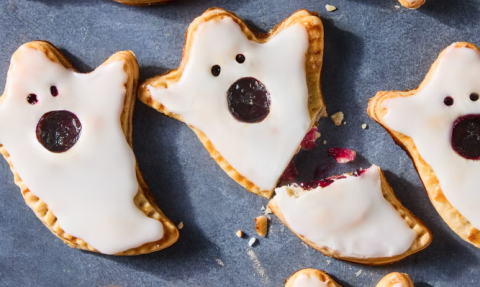 Iced hand pies made in the shape of ghosts. The ghosts' eyes and mouths show the blueberry jam inside the pie crust.