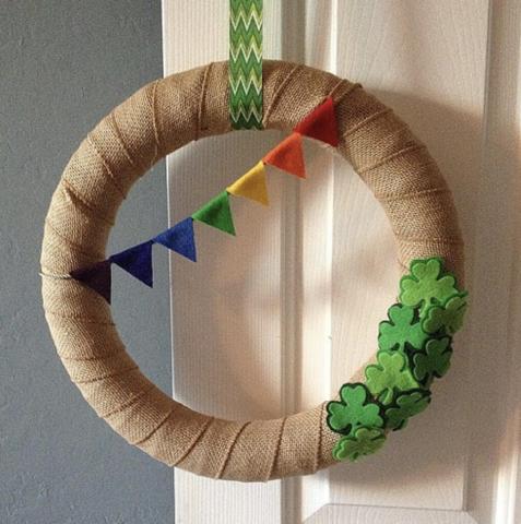A wreath ring covered in burlap ribbon with small felt shamrocks on one side and a banner made of rainbow felt triangles on the other.